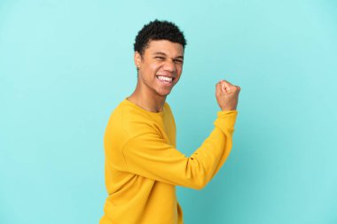 Genç Afrikalı Amerikalı bir adam mavi arka planda izole edilmiş zaferi kutluyor.