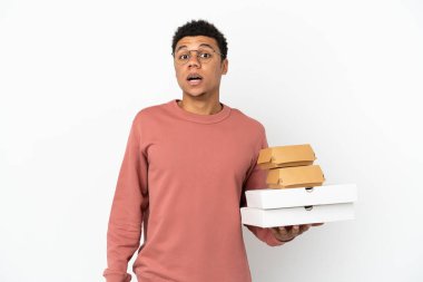 Young African American man holding a burger and pizzas isolated on white background with surprise facial expression