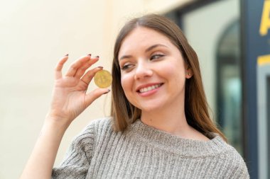 Genç, güzel sarışın kadın elinde mutlu bir ifadeyle Bitcoin tutuyor.