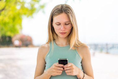 Açık havada cep telefonu kullanan genç sarışın kadın.