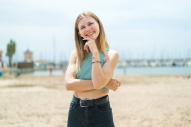 Açık havada gülümseyen genç sarışın kadın.