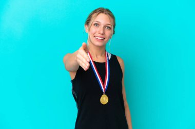 Mavi arka planda izole edilmiş, iyi bir anlaşma yaptığı için tokalaşan beyaz madalyalı genç bir kadın.