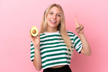 Pembe arka planda izole edilmiş avokado tutan beyaz bir kadın harika bir fikre işaret ediyor.