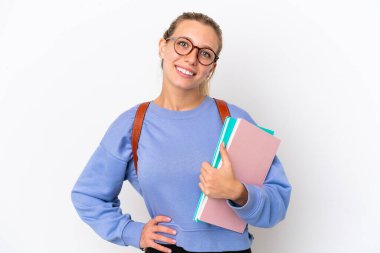 Beyaz arka planda izole edilmiş genç beyaz bir kadın kolları kalçasında ve gülümsüyor.