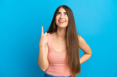 Mavi arka planda izole edilmiş genç beyaz kadın yukarı bakıyor ve şaşırıyor.