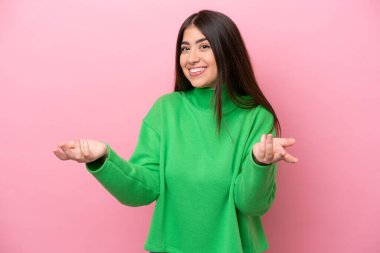 Pembe arka planda izole edilmiş genç beyaz kadın mutlu ve gülümsüyor.