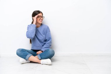 Beyaz arka planda izole bir şekilde yerde oturan beyaz bir kadın gülüyor.