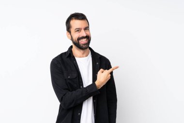 İzole edilmiş beyaz arka planı olan sakallı genç bir adam bir ürün sunmak için kenarı işaret ediyor.