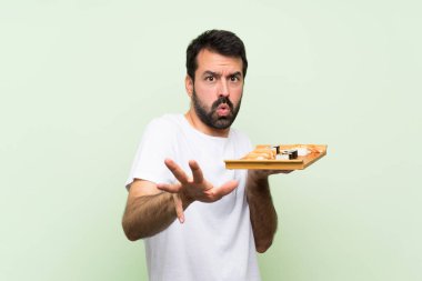 Yeşil duvarın üstünde suşisi olan genç yakışıklı bir adam gergin bir şekilde ellerini öne uzatıyor.