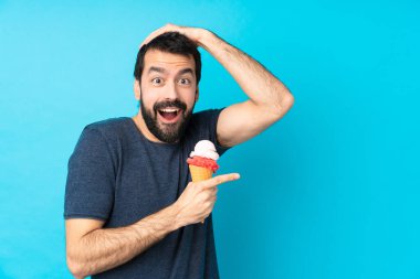 Kornet dondurması olan genç bir adam mavi arka planda şaşırmış ve parmağını kenarı işaret ediyor.