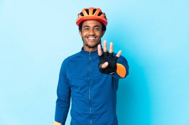 Arka planda örgü ören genç bisikletçi mutlu ve parmaklarıyla dört kişi sayıyor.