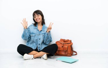 Beyaz arka planda tek başına oturan genç bir bayan yediyi parmaklarıyla sayıyor.