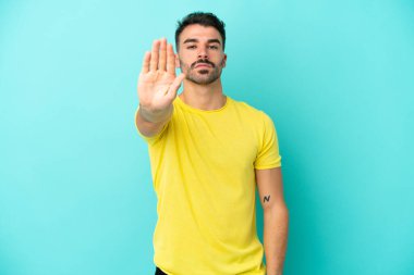 Mavi arka planda izole edilmiş genç beyaz adam dur hareketi yapıyor.