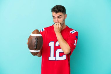 Rugby oynayan Kafkasyalı genç adam mavi arka planda izole edilmiş. Şüpheleri var.