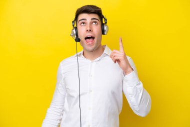 Tele pazarlamacı beyaz adam sarı arka planda izole edilmiş bir kulaklıkla çalışıyor.