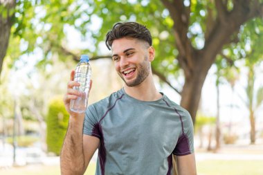 Açık havada bir şişe su ve neşeli bir ifadeyle genç yakışıklı sporcu.