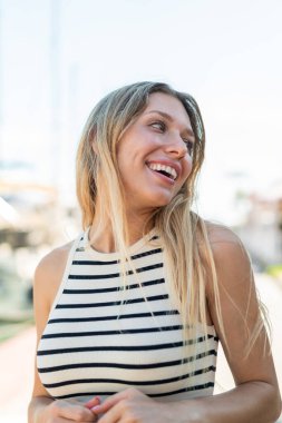 Açık havada genç sarışın bir kadın Neşeli bir ifadeyle