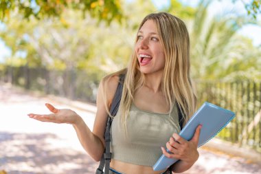 Açık havada, yüzünde sürpriz bir ifade olan sarışın genç bir bayan öğrenci.
