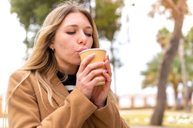 Genç, güzel, sarışın bir kadın açık havada kahve ikram ediyor.