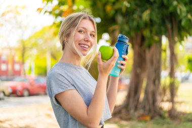 Genç sarışın kadın, açık havada bir elma ve bir şişe suyla.
