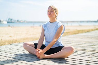 Açık havada yoga yapan genç sarışın kadın.