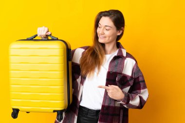 Genç İrlandalı kadın sarı arka planda izole edilmiş seyahat valiziyle tatilde.