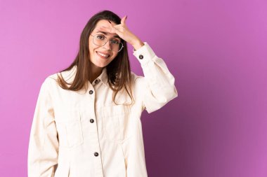 İzole edilmiş mor arka planı olan genç bir kadın bir şeye bakmak için çok uzaklara bakıyor.