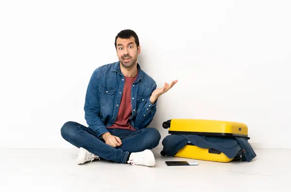 stock image Caucasian handsome man with a suitcase full of clothes sitting on the floor at indoors making doubts gesture