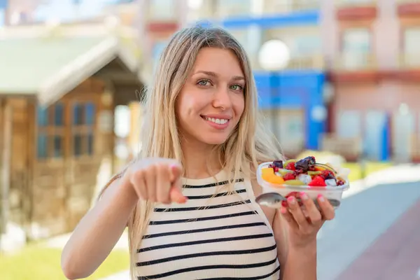 Young Blonde Woman Holding Bowl Fruit Outdoors Points Finger You — Stock Photo, Image