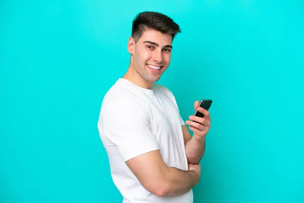 Jeune Homme Caucasien Isolé Sur Fond Bleu Tenant Téléphone Portable Image En Vente
