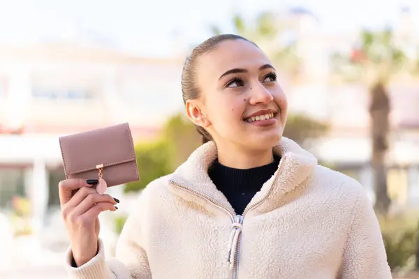 Young Moroccan Girl Holding Wallet Outdoors Looking While Smiling Лицензионные Стоковые Изображения