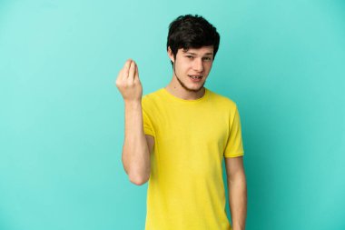Mavi arka planda izole edilmiş genç bir Rus İtalyan jesti yapıyor.