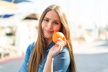 Açık havada elinde portakal tutan genç bir kadın.