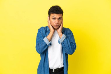 Sarı arka planda izole edilmiş genç Afrikalı Amerikalı hayal kırıklığına uğramış ve kulaklarını kapatmış.