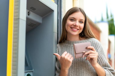 Genç, sarışın bir kadın ATM kullanıyor.