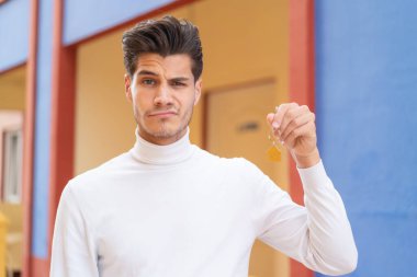 Kafkasyalı genç bir adam evinin anahtarlarını üzgün bir ifadeyle tutuyor.