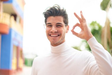 Dışarıdaki genç beyaz adam gözlüklü ve tamam işareti yapıyor.