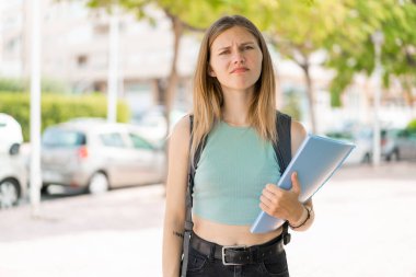 Dışarıda üzgün bir ifadeyle sarışın genç bir bayan öğrenci.