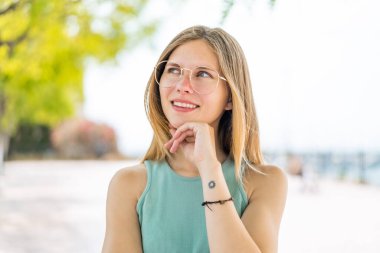 Açık havada genç sarışın bir kadın Gözlüklü ve düşünürken yukarı bakarken