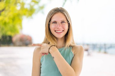 Açık havada, gözlüklü ve işaret eden genç sarışın kadın.