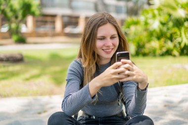 Açık havada cep telefonu kullanan genç sarışın kadın.