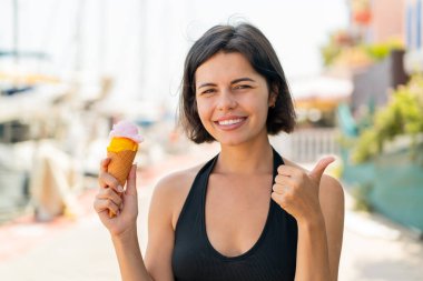 Açık havada kornet dondurmalı genç ve güzel bir Bulgar kadın. Başparmakları havada, çünkü iyi bir şey oldu.