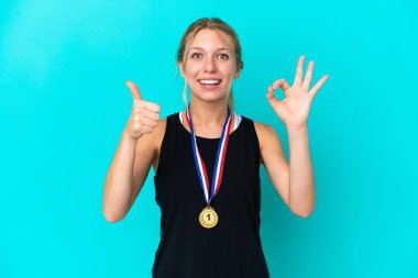 Mavi arka planda madalyaları olan genç beyaz kadın işaret ve işaret dilini gösteriyor.