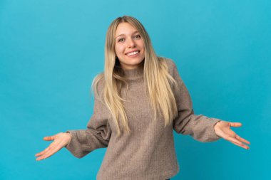 Mavi arka planda izole edilmiş genç sarışın kadın mutlu ve gülümsüyor.