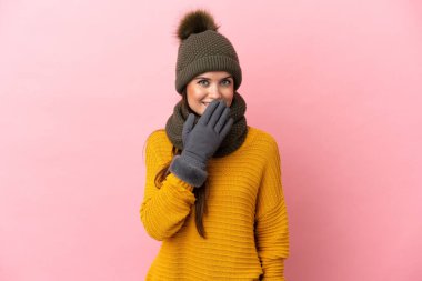 Kışlık şapkalı genç beyaz kız pembe arka planda izole edilmiş mutlu ve ağzı kapalı gülümsüyor.