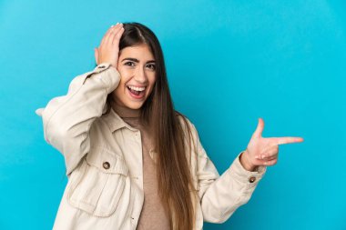 Mavi arka planda izole edilmiş genç beyaz kadın şaşırdı ve işaret etti.