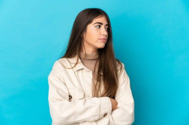 Mavi arka planda izole genç beyaz kadın kollarını çapraz tutuyor.