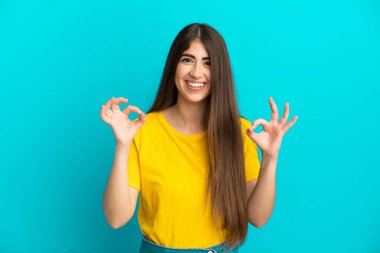 Mavi arka planda izole edilmiş beyaz bir kadın iki eliyle tamam işareti gösteriyor.