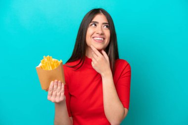 Kızarmış patates yakalayan beyaz bir kadın mavi arka planda izole edilmiş gülümserken yukarı bakıyor.