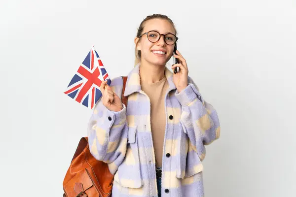 stock image Young blonde woman holding an United Kingdom flag isolated on white background keeping a conversation with the mobile phone
